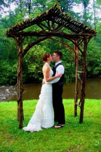 wet wedding kiss under hand made wooden arch in front of river